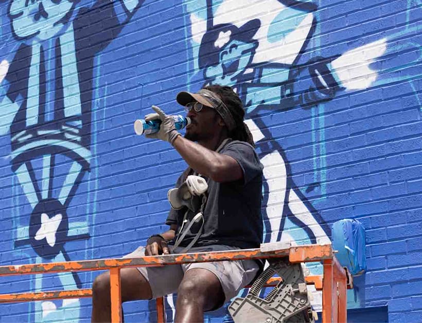 Deer Park Artist George F. Baker III, aka GFB3, taking a break with Deer Park spring water while painting a mural of his bottle art.